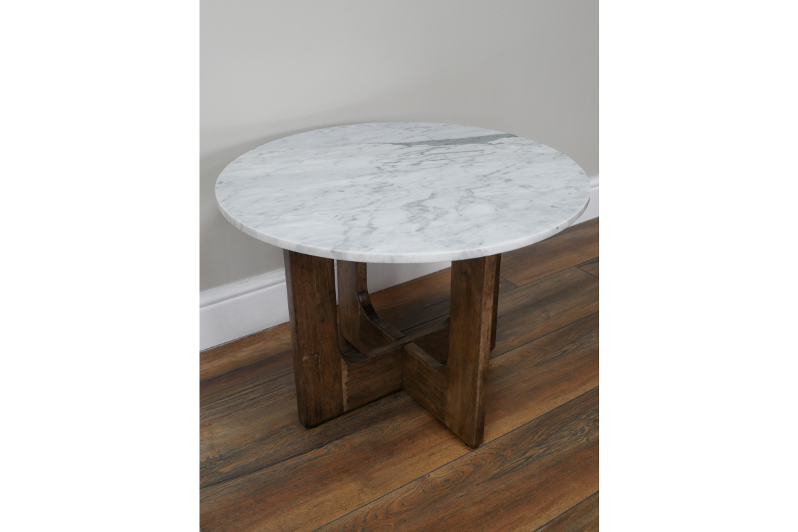 Round side table with white marble top and dark wooden legs on wooden floor, angled view.