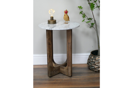 Small side table with round white marble top and dark wooden crossed legs, shown with lamp and decorative bird on top.