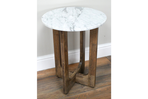 Small round side table with white marble top and three brown wooden legs, shown at slight angle on wood floor.