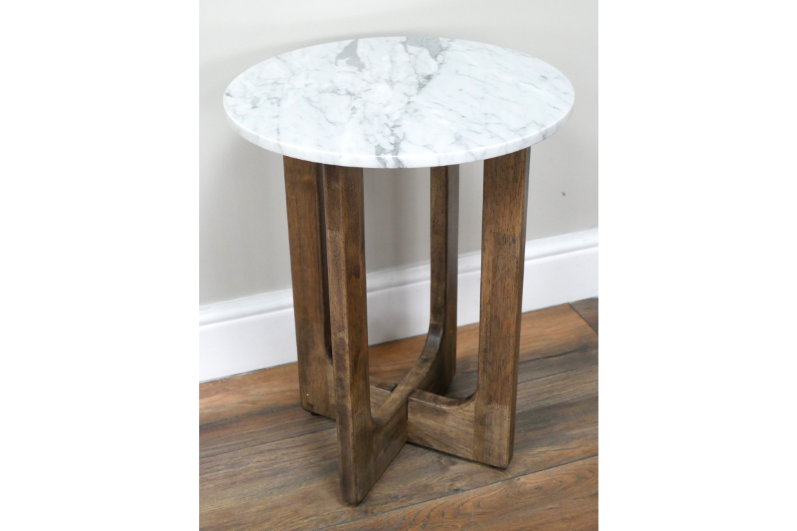 Small round side table with white marble top and three brown wooden legs, shown at slight angle on wood floor.
