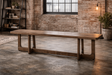 Long wooden bench with thick top and sturdy legs, shown at an angle in an industrial loft setting.