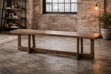 Long wooden bench with thick top and sturdy legs, shown at an angle in an industrial loft setting.