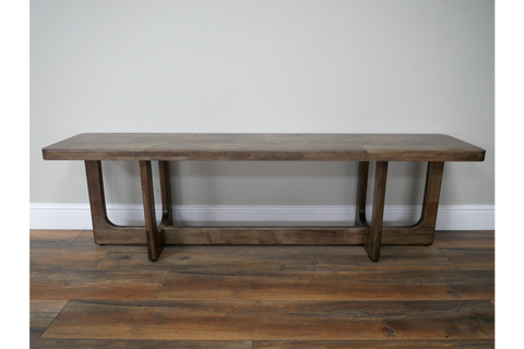 Long wooden bench with a rectangular top and U-shaped legs, shown from the front on wooden flooring.