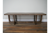 Long wooden bench with a rectangular top and U-shaped legs, shown from the front on wooden flooring.