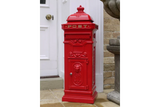 red cast iron post box with gold lettering beside white door and brick wall