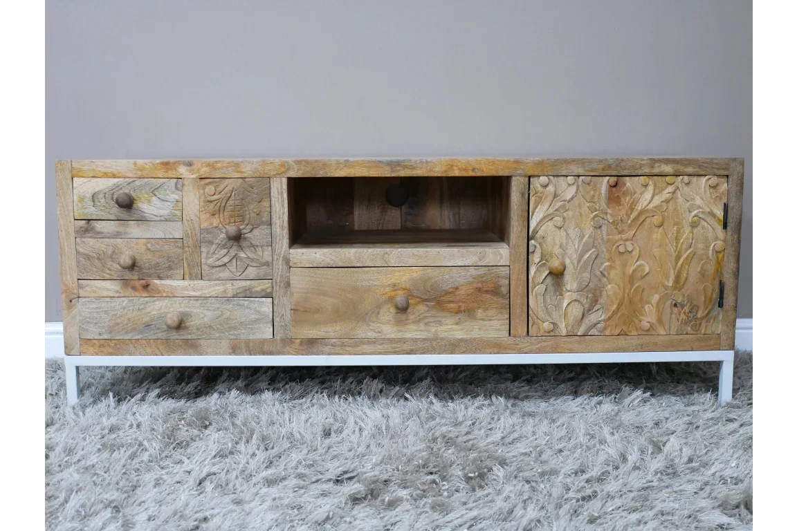 Mango wood TV unit with carved floral doors, storage drawers, and open shelf on white legs