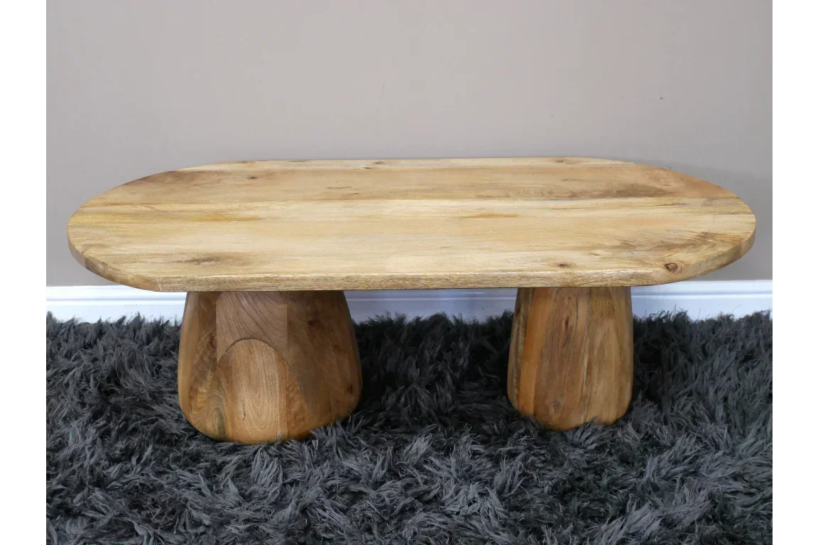 Solid wood coffee table with oval top and chunky legs on grey rug