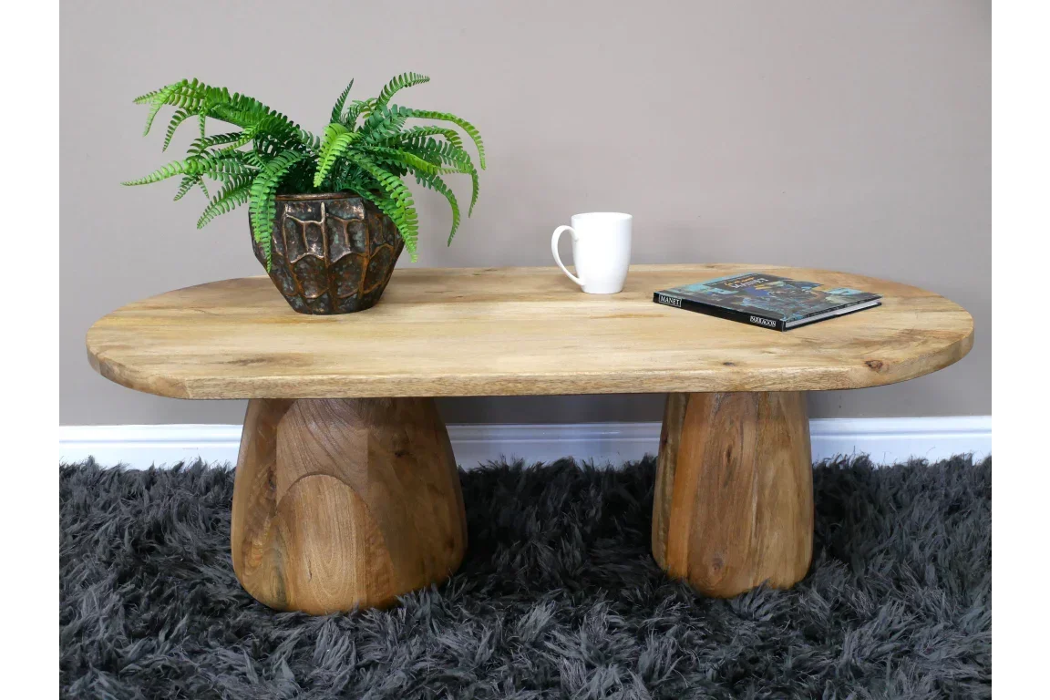 Solid wood coffee table with oval top, plant in pot, mug, and book on grey shaggy rug