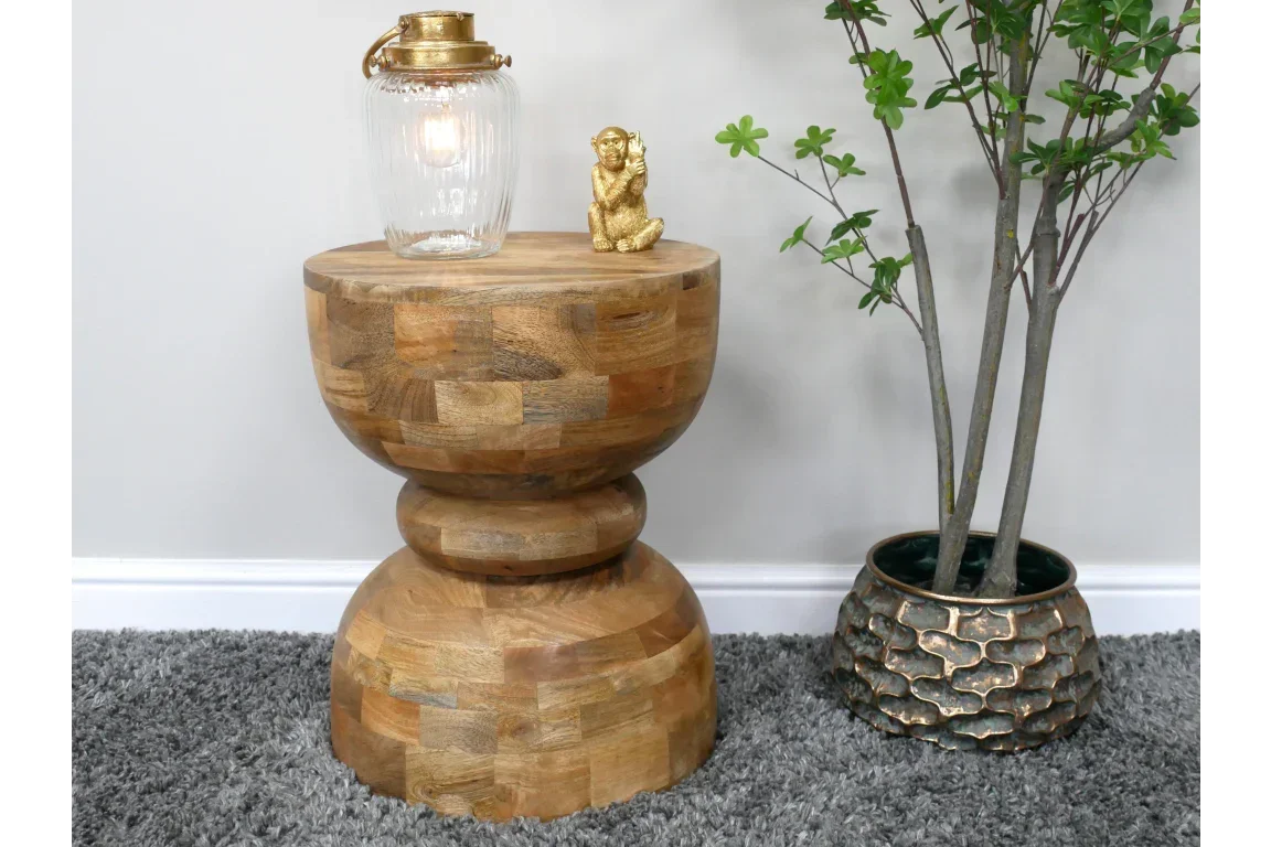 Round wood side table with decorative lamp and gold ornament beside potted plant