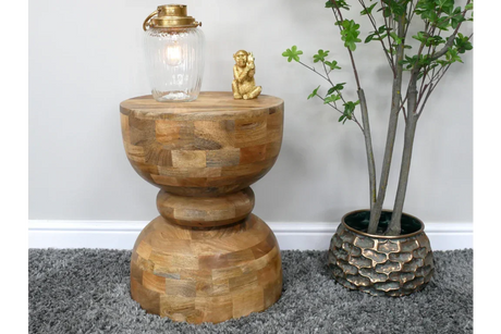 Round wood side table with decorative lamp and gold ornament beside potted plant