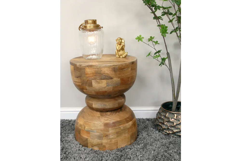 Solid wood side table with rounded base, lamp, gold ornament, grey rug and indoor plant