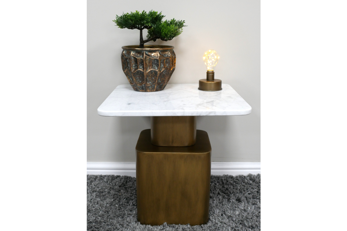 Square side table with white marble top and bronze metal base, decorated with a small plant and light bulb on top.