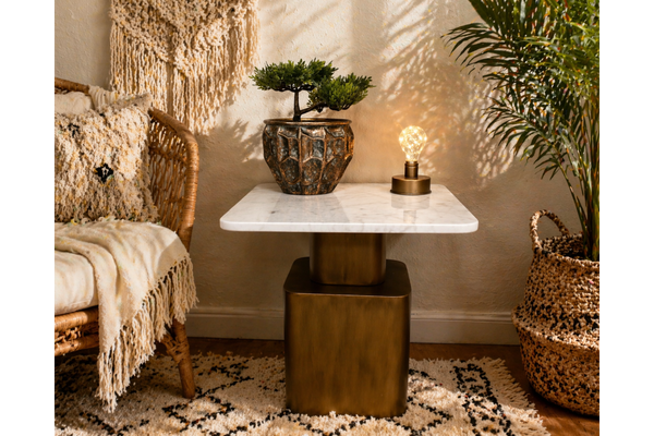 Square side table with white marble top and bronze metal base in cozy room setting, shown from front angle.