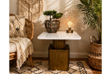 Square side table with white marble top and bronze metal base in cozy room setting, shown from front angle.