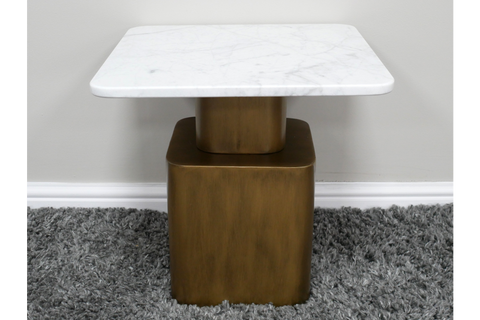 Square side table with white marble top and bronze metal base on gray shag carpet against white wall.
