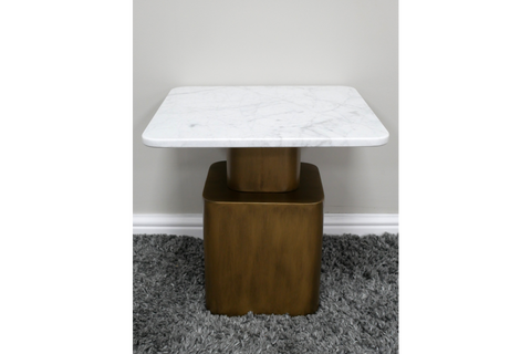 Square side table with white marble top and bronze metal base on gray shag carpet, front view.