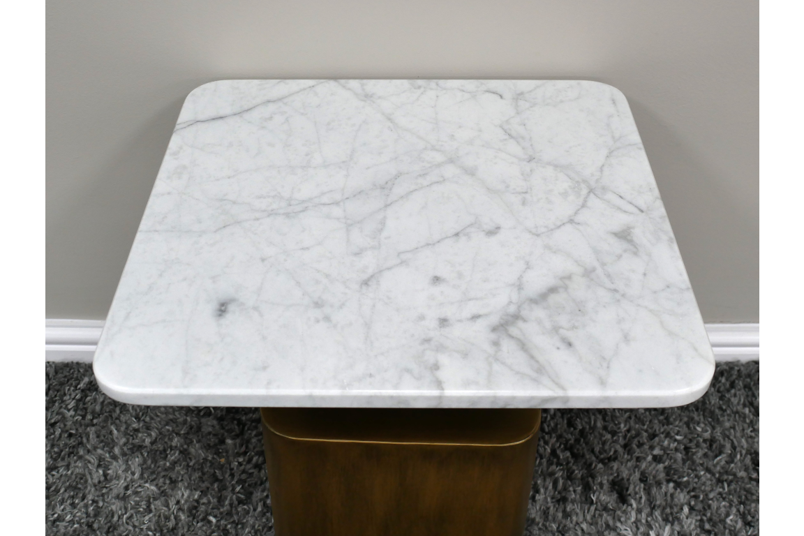 Square side table with white marble top and rounded corners, brass-colored base, viewed from above on dark carpet.