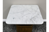 Square side table with white marble top and rounded corners, brass-colored base, viewed from above on dark carpet.