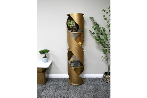 Tall gold metal swirl display cabinet with three shelves, shown in a minimalist room setting from the front angle.