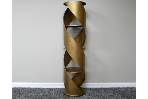 Tall swirl display cabinet in bronze metal with spiral design and three shelves, standing against a plain wall on gray