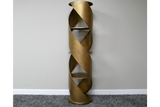 Tall swirl display cabinet in bronze metal with spiral design and three shelves, standing against a plain wall on gray