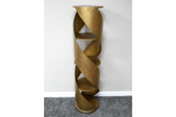Tall spiral display cabinet in brass-colored metal with circular shelves, shown from front angle against white wall.