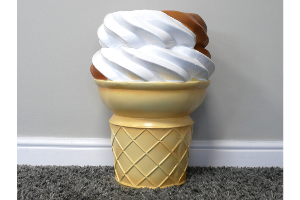 Ice cream cone-shaped side table with white and brown swirl top, yellow cone base, photographed on gray carpet near wall