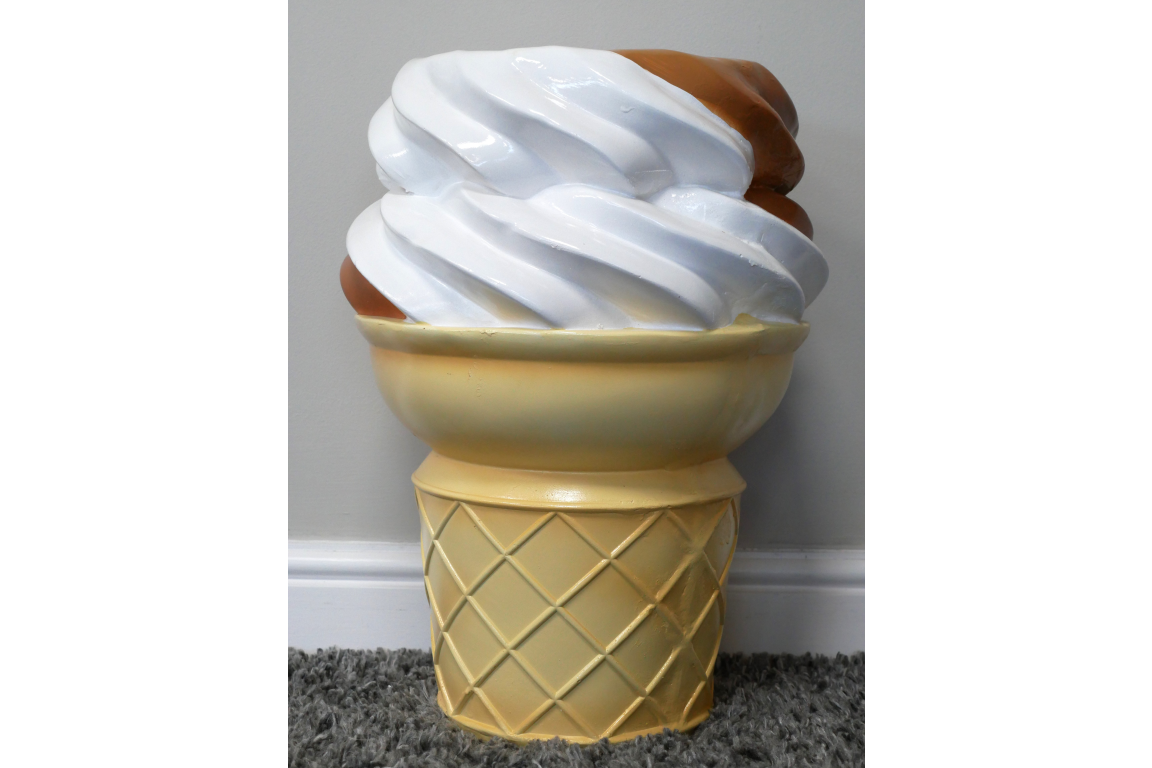 Beige and white plastic side table shaped like a soft serve ice cream cone, shown from the front on a carpeted floor.