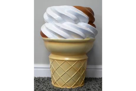 Beige and white plastic side table shaped like a soft serve ice cream cone, shown from the front on a carpeted floor.