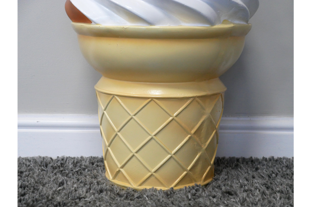 Yellow ceramic side table shaped like an ice cream cone base with a white swirl top, shown from front angle on carpet.