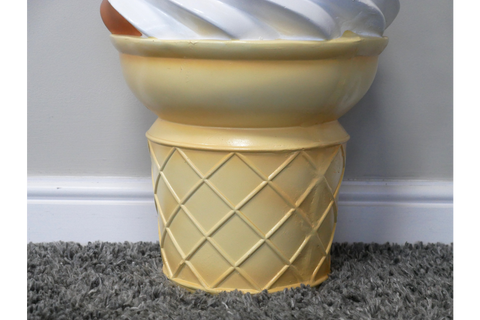 Yellow ceramic side table shaped like an ice cream cone base with a white swirl top, shown from front angle on carpet.
