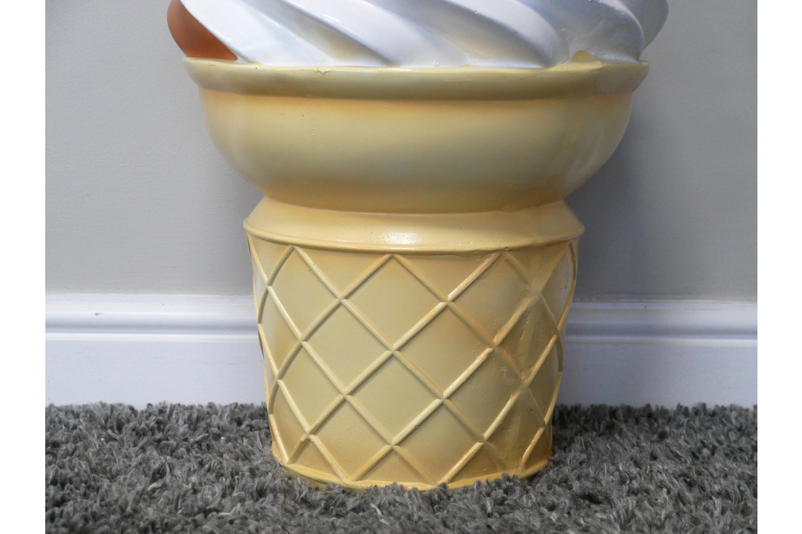 Yellow ceramic side table shaped like an ice cream cone base with a white swirl top, shown from front angle on carpet.