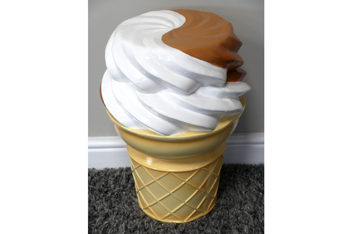 Plastic ice cream cone-shaped side table in beige, white, and brown, shown from a high front angle on carpet.