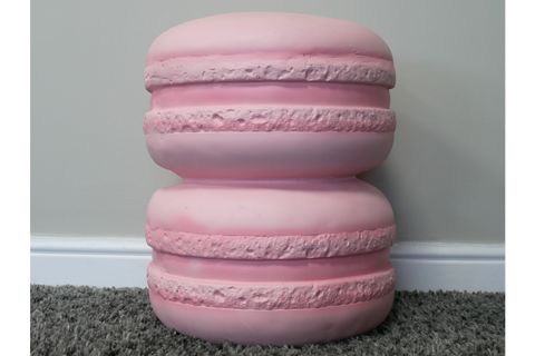 Pink resin side table shaped like two stacked macarons, front view on grey carpet and white baseboard background.