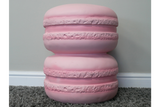 Pink resin side table shaped like two stacked macarons, front view on grey carpet and white baseboard background.