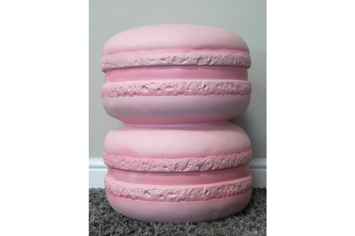 Pink macaron-shaped side table with textured detailing, photographed from front on a gray carpet floor against pale wall.