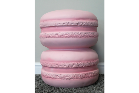 Pink macaron-shaped side table with textured detailing, photographed from front on a gray carpet floor against pale wall.