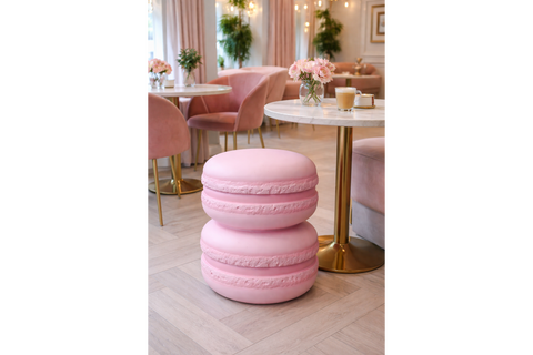 Pink macaron-shaped side table with a smooth matte finish, set on light wooden floor near a round marble top table.