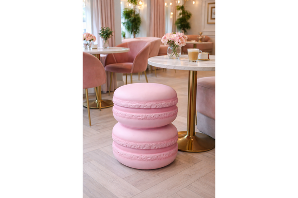 Pink macaron-shaped side table with a smooth matte finish, set on light wooden floor near a round marble top table.