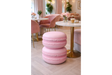 Pink macaron-shaped side table with a smooth matte finish, set on light wooden floor near a round marble top table.