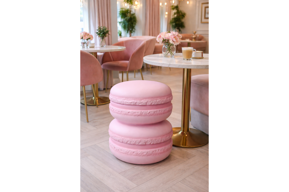 Pink macaron-shaped side table with a smooth matte finish, set on light wooden floor near a round marble top table.