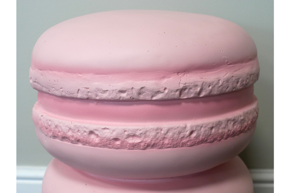 Pink macaron-shaped side table with textured matte finish, shown in close-up against a pale wall background.
