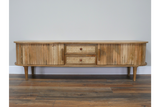 Wooden TV cabinet with rounded edges, slatted doors, cane drawer fronts, and tapered legs, front view.