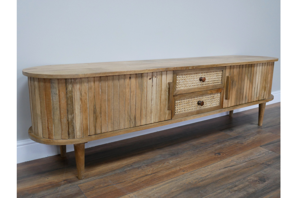 Wooden TV cabinet with rounded edges, vertical slat detailing, two woven drawer fronts, angled front view on wooden floor.