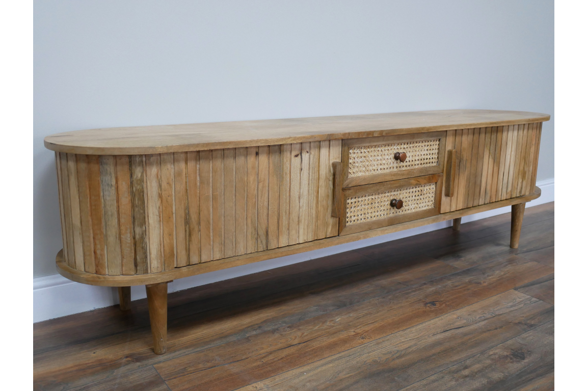 Wooden TV cabinet with rounded edges, vertical slat detailing, two woven drawer fronts, angled front view on wooden floor.