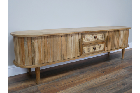 Wooden TV cabinet with rounded edges, vertical slat detailing, two woven drawer fronts, angled front view on wooden floor.