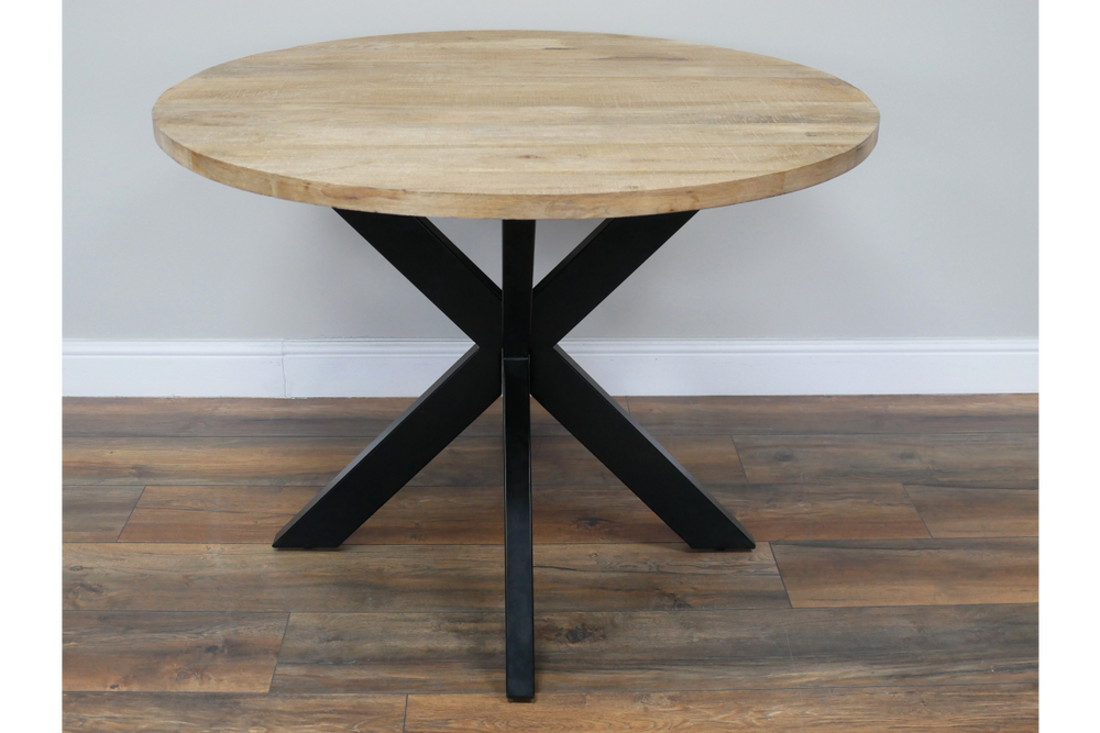 Round wooden dining table with light natural finish and black metal X-shaped base, front angle view on wooden floor.