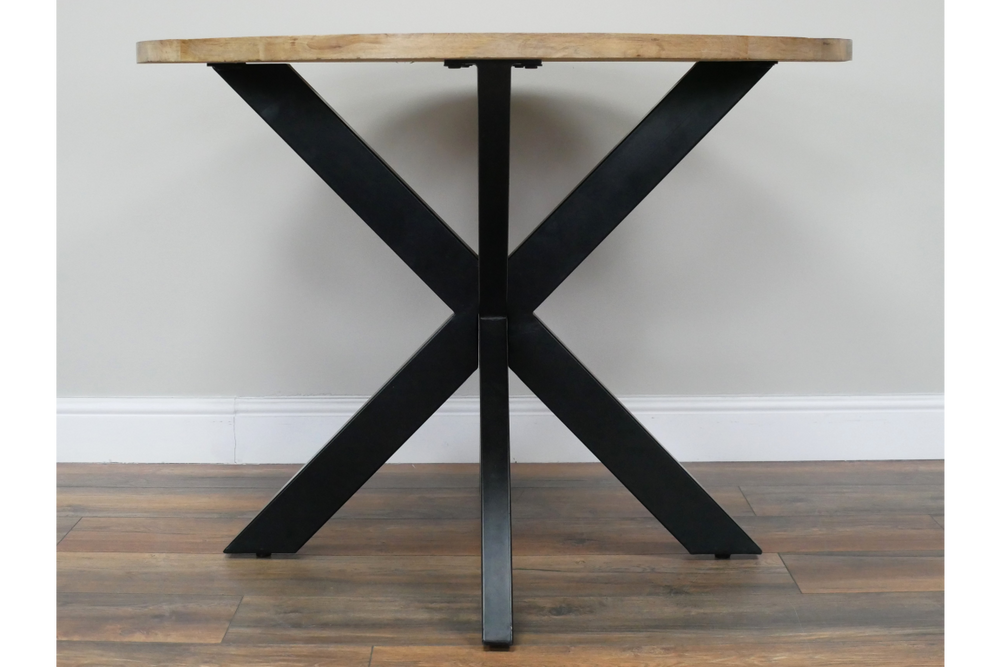 Round dining table with light wood top and black metal X-shaped base, front view on wooden floor.