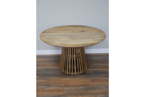 Round wooden dining table with slatted base, natural finish, front view on wooden floor against gray wall.