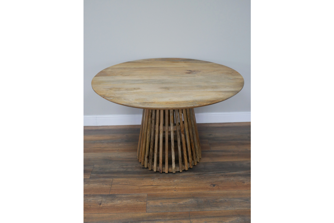 Round wooden dining table with slatted base, natural finish, front view on wooden floor against gray wall.